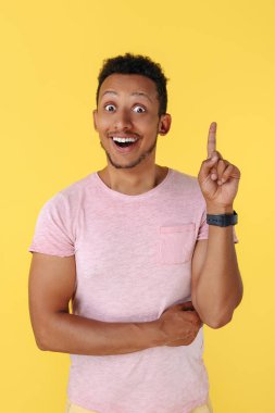 Şaşırmış Afrikalı Amerikalı genç adam sarı arka plan üzerinde parmağını kaldırıyor. Fikir kavramı.