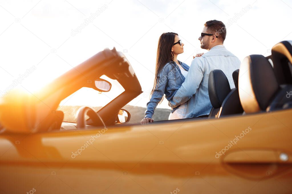 Lovely young couple hugging beside a convertible car. Freedom, travel and love concept.