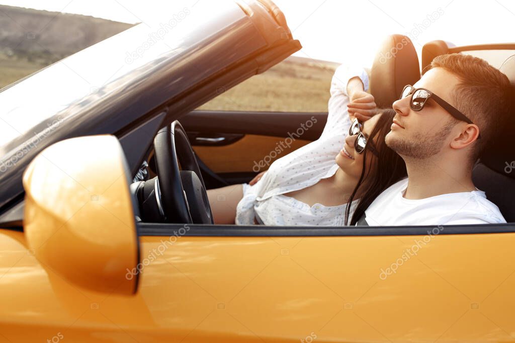 Modern young couple going on a long drive in a convertible car on the sunset. Freedom, travel and love concept.