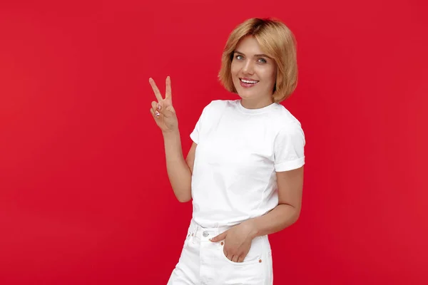 Ganska ung blond kvinna i casual vit outfit visar fred gest över röd bakgrund. — Stockfoto