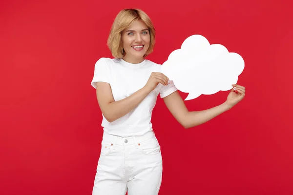 Smiling young blonde woman holding blank speech bubble over red background. — Stock Photo, Image