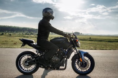 Motosikletlinin gün batımında şehir yolunda motosiklet üstünde oturduğu fotoğraf..
