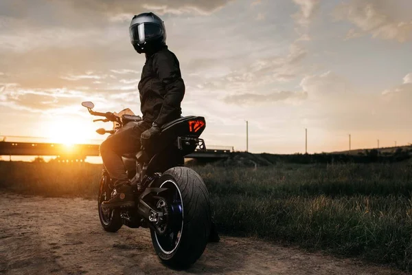 Baksidan av cyklist sitter på motorcykel i solnedgången på landsvägen. — Stockfoto