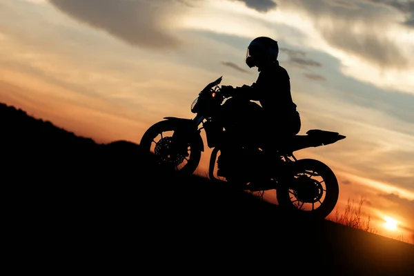 Silhuett foto av cyklist kör motorcykel i solnedgången på den bergiga vägen. Framgång och seger koncept. — Stockfoto