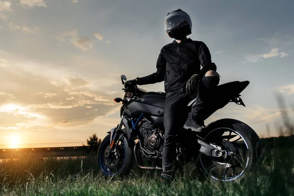 Foto de motociclista sentado en motocicleta al atardecer en la carretera del campo. —  Fotos de Stock
