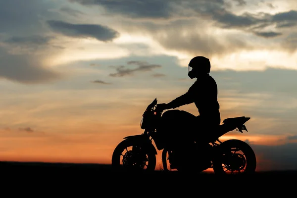 Silhuett foto av cyklist körning motorcykel i solnedgången på landsvägen. — Stockfoto