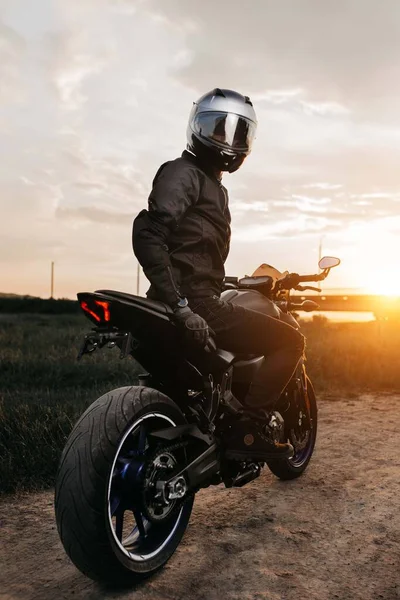 Imagen dramática del motociclista sentado en motocicleta al atardecer en la carretera del campo. —  Fotos de Stock