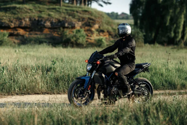 Foto de motociclista sentado en motocicleta al atardecer en la carretera del campo. —  Fotos de Stock