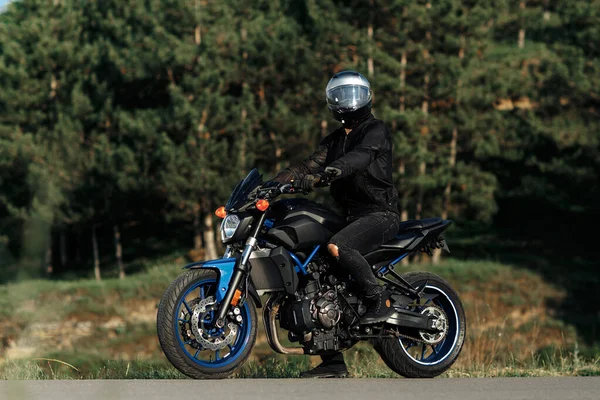 Foto de motociclista sentado en motocicleta al atardecer en la carretera del campo. —  Fotos de Stock