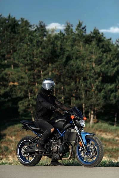 Foto de motociclista sentado en motocicleta al atardecer en la carretera del campo. —  Fotos de Stock