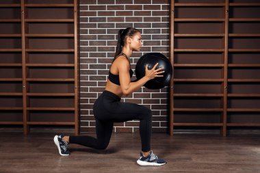 Formda genç esmer kadın spor salonunda tıp topuyla hiç bir şey yapmıyor..