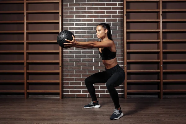Sporcu genç esmer kadın spor salonunda tıp topuyla çömelmiş egzersiz yapıyor.. — Stok fotoğraf