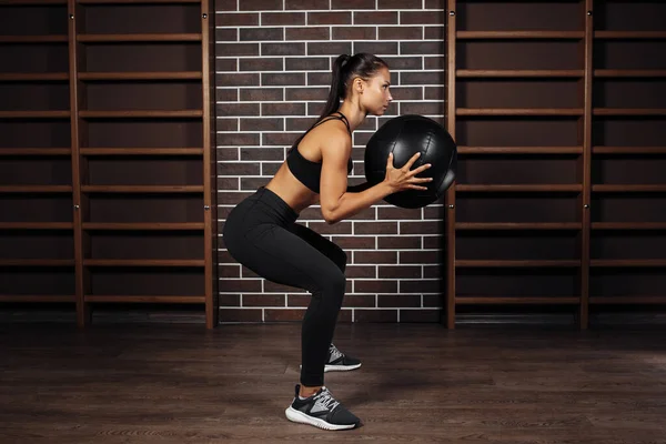 Fit junge brünette Frau macht Kniebeuge mit Medizinball im Fitnessstudio. — Stockfoto