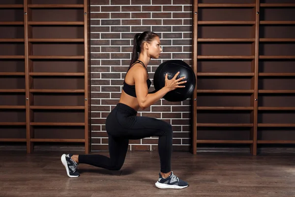Přizpůsobit mladé brunetky žena dělá squat cvičení s medicínou míč v tělocvičně. — Stock fotografie
