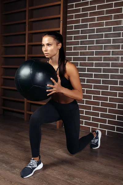 Přizpůsobit mladé brunetky žena dělá squat cvičení s medicínou míč v tělocvičně. — Stock fotografie