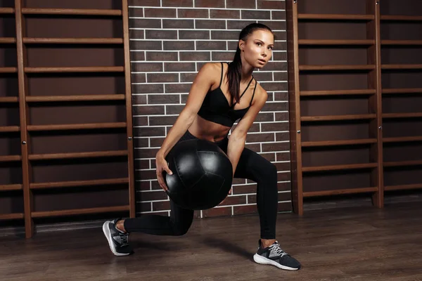 Atraktivní fit mladá brunetka žena cvičení s medicínou míč v tělocvičně. — Stock fotografie