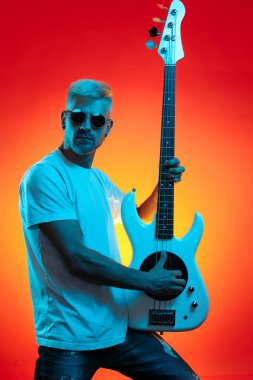 Kendine güvenen sarışın hippi, neon ışıklarla beyaz bas gitar çalıyor. Rock müzik konsepti.