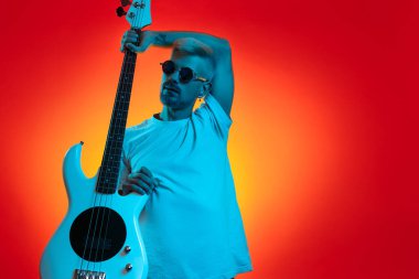 Sarışın modaya uygun hippi elinde bas gitarla neon ışıklarla poz veriyor. Rock müzik konsepti.