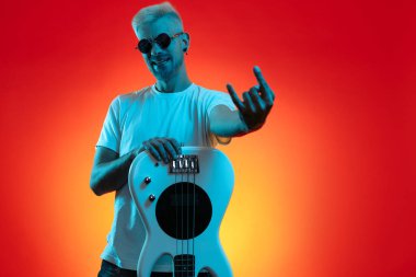 Kendine güvenen hippi beyaz bas gitar tutuyor ve neon ışıklarda rock hareketi yapıyor. Rock müzik konsepti.