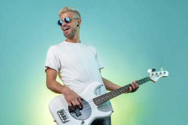 Neşeli hipster adam neon ışıklarda beyaz bas gitar çalar. Rock müzik konsepti. Rock yıldızı.