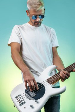 Ciddi hipster adam neon ışıklarda beyaz bas gitar çalıyor. Rock müzik konsepti. Rock yıldızı.