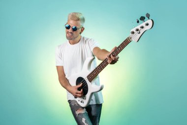 Yakışıklı hippi, neon ışıklarla beyaz bas gitar çalıyor. Rock müzik konsepti. Rock yıldızı.