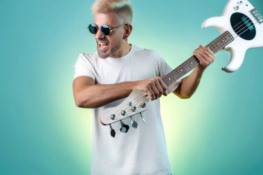 Havalı sarışın hippi beyaz gitarı neon ışıklarla eziyor. Rock müzik konsepti.