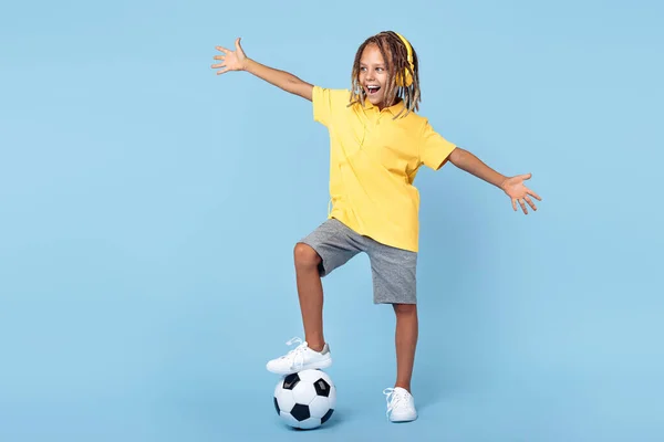 一个快乐的小男孩，带着耳机，用蓝色背景的足球抱住一条腿. — 图库照片