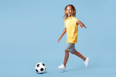 Afrika korkusu olan mutlu küçük çocuk mavi arka planda futbol topu atıyor..