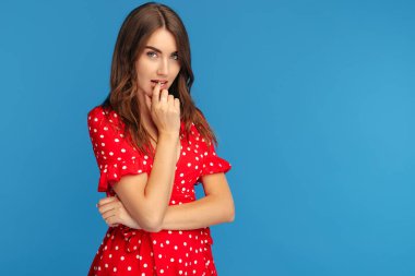 Kırmızı elbiseli, parlak gülüşlü güzel bir kadın mavi arka planda poz veriyor..