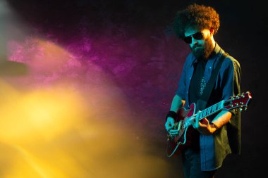 Neon ışıklı kırmızı gitarlı şık hippi adam. Rock müzisyeni elektro gitar çalıyor..