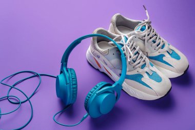 Mor arka planda şık mavi kulaklık ve spor ayakkabılar. Müzik konsepti.