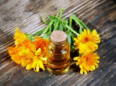 Ahşap arka planda kadife çiçekli kadife yağı şişesi. Calendula çiçeği.