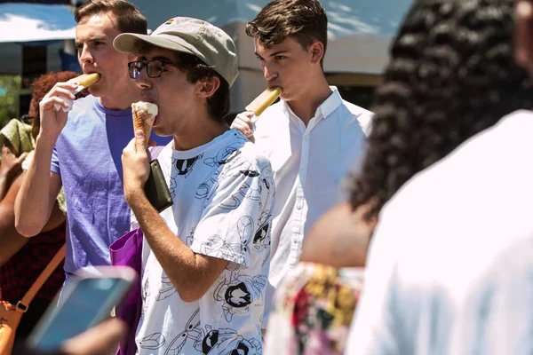 Los hombres jóvenes caminan y comen helado en el festival de verano — Foto de Stock
