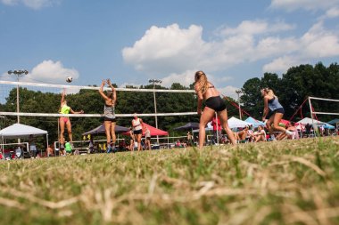 Low Angle Young Women Competing In Triples Grass Volleyball Tournament clipart