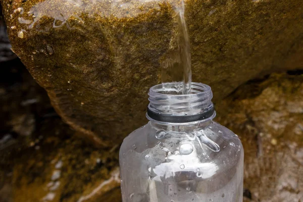 A person pours water into a bottle of mountain stream.