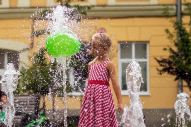 Lviv, Ukrayna - Ağustos 2019. Kırmızı elbiseli bir kız şehir meydanındaki fıskiyede yeşil bir balonla oynuyor..