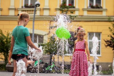 Lviv, Ukrayna - Ağustos 2019. İki kız şehir meydanında bir çeşme yeşil bir balon ile oynuyor.