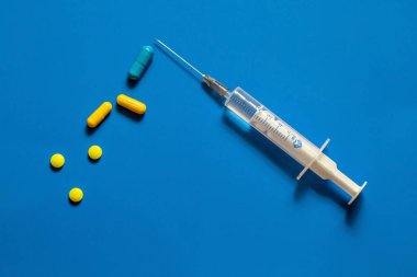 Farklı renkli ilaç hapları, kapsüller ve şırınga. Kavram: enjeksiyon veya hap? Mavi arka plan.