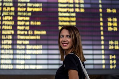 Havaalanında zaman çizelgesinin önünde küçük bir sırt çantası olan bir kız uçuşu bekliyor..