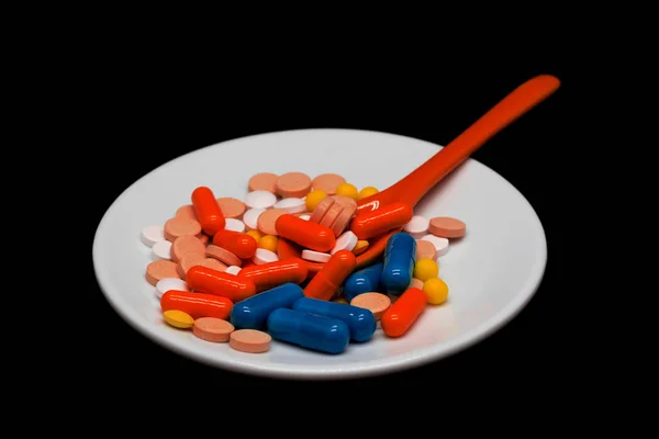異なる色の医薬品の錠剤やカプセルとプレート内のカプセルとスプーン 暗い光と黒い背景 — ストック写真