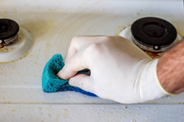 Beyaz lastik eldivenli bir el kirli bir tencereyi sünger ve köpüklü deterjanla yıkar..