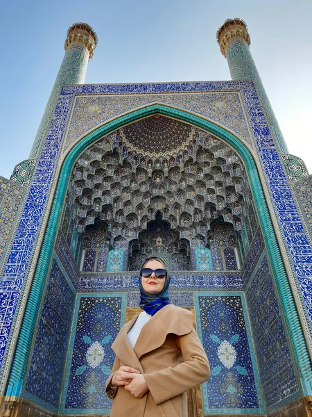 A girl in a coat and a blue handkerchief stands before entrance to the Shah Mosque in the Naghsh-e Jahan Square.