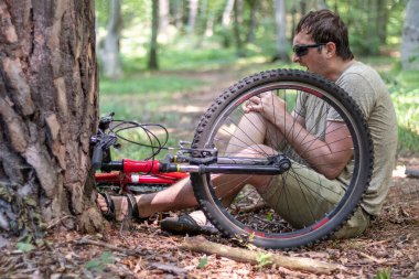 Bisiklet sürerken bir kaza. Ormanda bisikletten düştükten sonra diz ağrısı çeken bir adam. Sigorta konsepti.