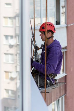 Bir işçi yüksek bir binanın pencerelerini yalıtır. İplere asılmış. Endüstriyel yükseklik.