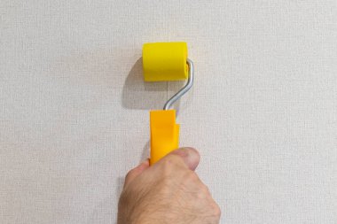 Adam lastik silindirle duvar kağıdı dikişlerini kapatıyor..