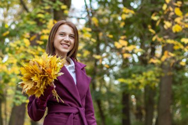 Sonbahar parkında yürürken gülümseyen genç bir kadının portresi.