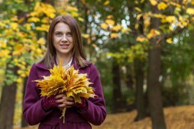 Parktaki kadın sonbahar yapraklarını tutuyor.