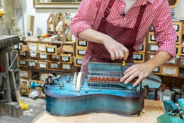 Craftsman repairs Hurdy-gurdy (wheel vielle) in workshop.