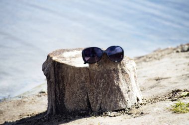 Güneş gözlüğü bir ağaç kütüğü üzerinde asılı, güneş vurgular ile nehrin bir arka plan üzerinde